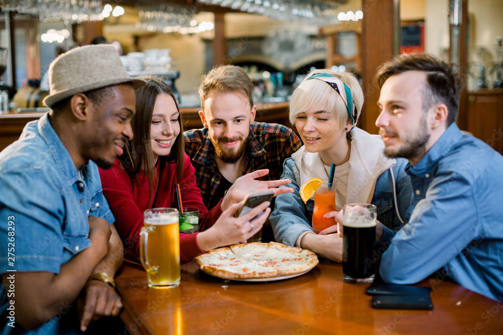 Group of young cheerful friends are sitting in a cafe, eating, drinking drinks. Friends take selfies and take pictures. Group of young cheerful friends are sitting in a cafe, eating, drinking drinks. Friends take selfies and take pictures.