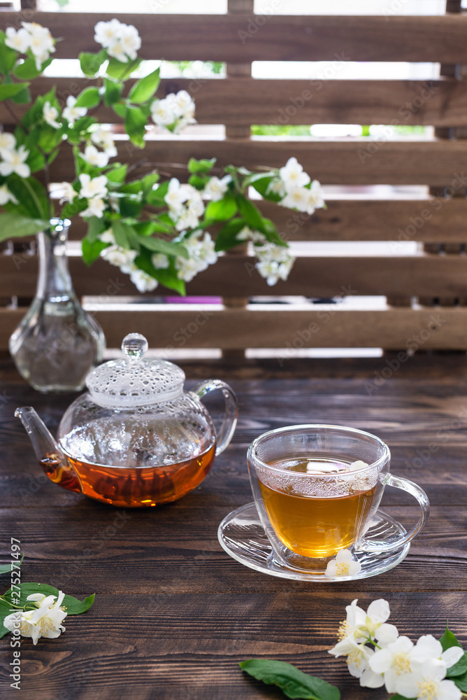 Jasmine tea in transparent cup, jasmine flowers and teapot on wooden table. Copy space. Tea party Jasmine tea in transparent cup, jasmine flowers and teapot on wooden table. Copy space. Tea party