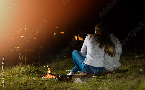 Happy couple in silhouette, sitting near a fire. Night sky with clouds. city lights on the background