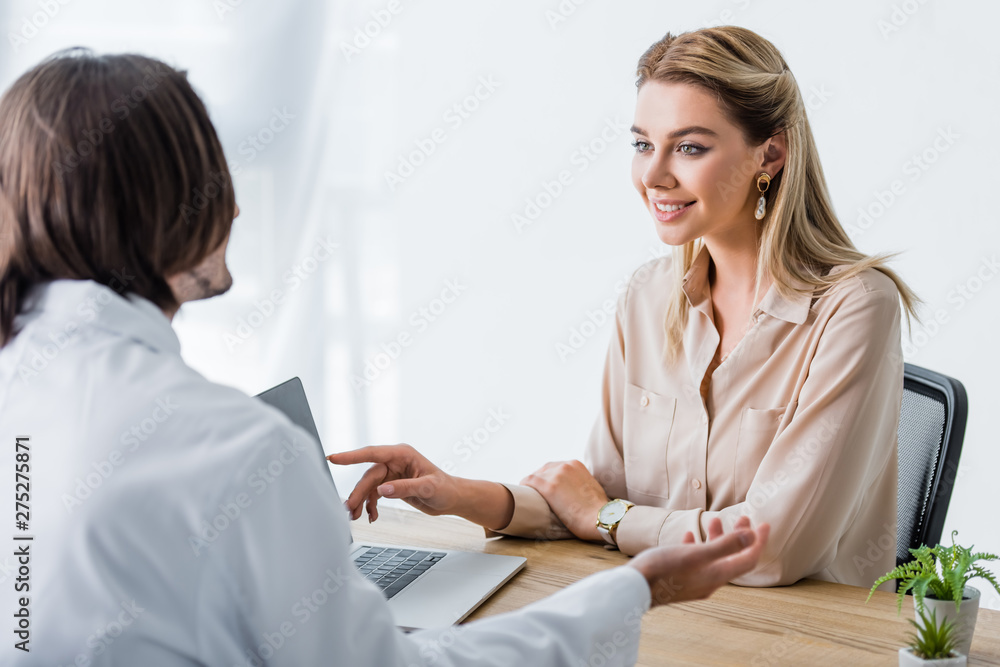 beautiful smiling patient looking at doctor and pointing with finger at laptop beautiful smiling patient looking at doctor and pointing with finger at laptop
