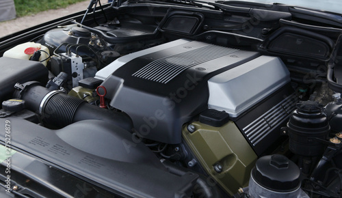 New modern powerful car engine close up view. Covered with black, silver, army green colored plastic. Big sizing, lots of tubes and wires, internal system mechanisms. Clean, smooth surface.