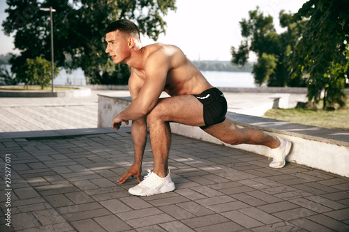 A muscular male athlete doing workout at the park. Gymnastics, training, fitness workout flexibility. Summer city in sunny day on background field. Active and healthy lifestyle, youth, bodybuilding. © master1305