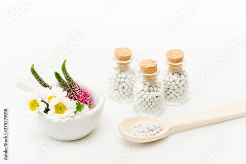 flowers in mortar near pestle and glass bottles with pills on white
