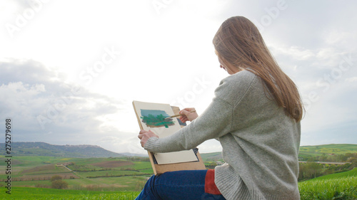 A young woman sits on the green field and drawing a painting photo