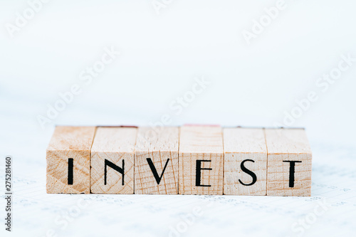 Investment, stock, bond or equity concept, pen and wooden stamp block arrange the word INVEST on asset price numbers table report paper on table with white copy space