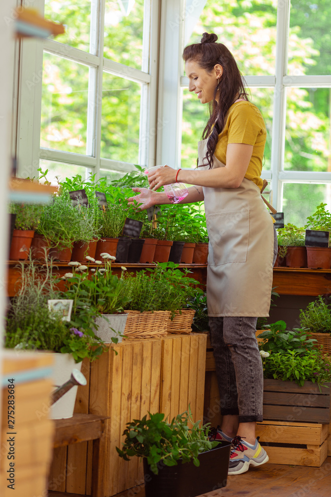 Focused florist carefully sprinkling flowers and smiling. Focused florist carefully sprinkling flowers and smiling.