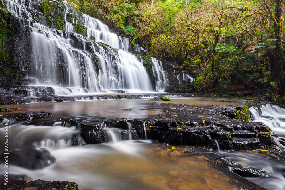 Purakaunui falls waterfall located in a serene forest. The Purakaunui Falls are a cascading three-tiered waterfall on the Purakaunui River, in The Catlins region of the South Island, New Zealand. Purakaunui falls waterfall located in a serene forest. The Purakaunui Falls are a cascading three-tiered waterfall on the Purakaunui River, in The Catlins region of the South Island, New Zealand.