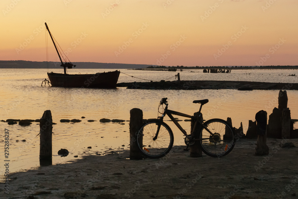 Landscape with water, old boat and bicicle at sunset.