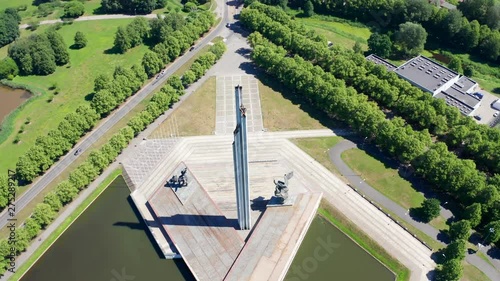 Aerial View Of Victory Monument In Riga (Uzvaras Piemineklis), Amazing Geometrical Cinematic Reveal Shot, Old Town Appearing photo