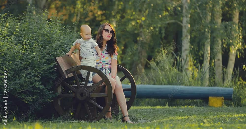 Summer walk in the park. Young mother is resting on the bench with her little son. Mom's rest with her son. Summer walk in the park. Young mother is resting on the bench with her little son. Mom's rest with her son.