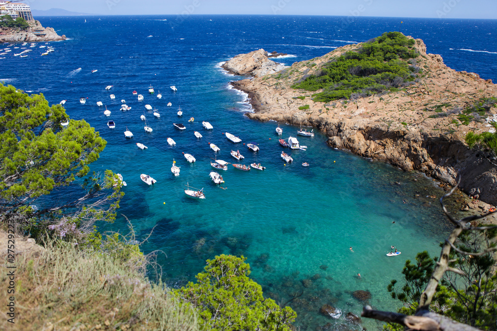 Costa brava sea cost in Spain. Clear water and boats and yachts. Horizon line and blue sky. Rocks and hills at the background. Summer vacations in Catalonia. 