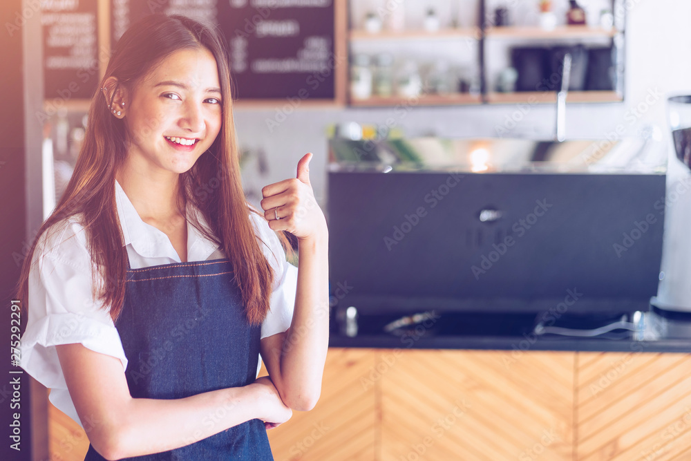 Pretty young asian waitress standing arms crossed in cafeteria.Coffee Business owner Concept.  barista in apron smiling at camera in coffee shop counter