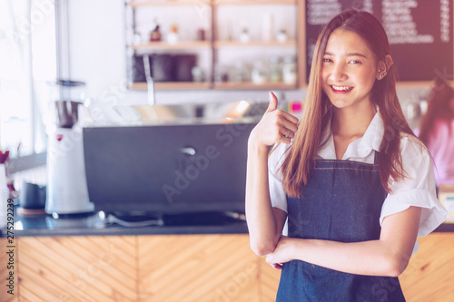 Pretty young asian waitress standing arms crossed in cafeteria.Coffee Business owner Concept. barista in apron smiling at camera in coffee shop counter