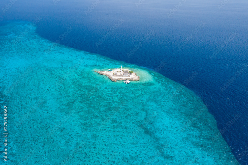 Aerial drone view of a lighthouse on a tiny tropical island surrounded by coral reef and deep water (Capitancillo Island, Cebu, Philippines)