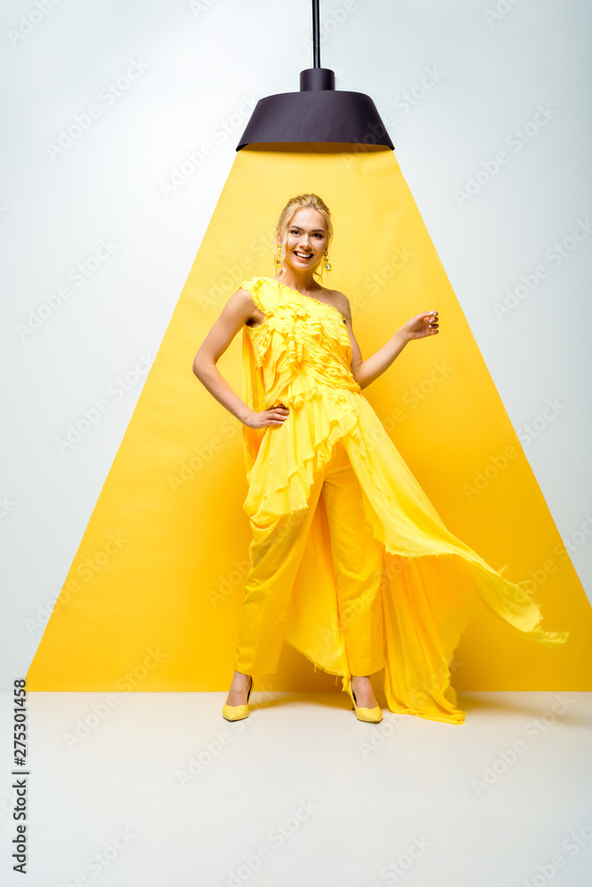 happy young woman standing with hand on hip and gesturing on white and yellow