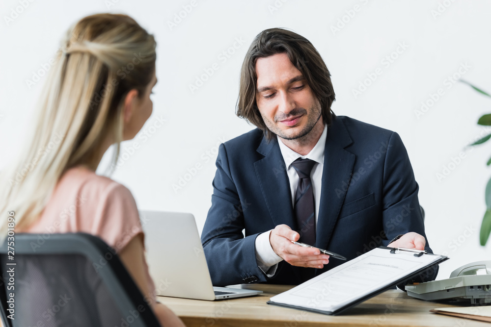 selective focus of handsome businessman talking with client while holding contract in hands selective focus of handsome businessman talking with client while holding contract in hands
