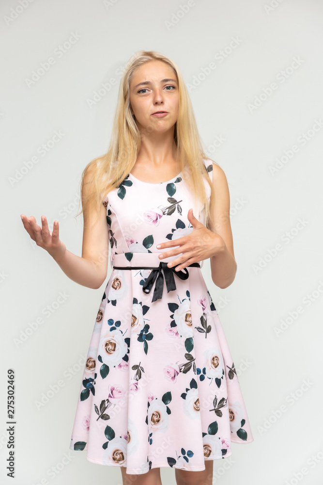 Portrait of a cute beautiful pretty woman girl with long beautiful hair on a white background in a pink dress with a pattern. Shows many different emotions, smiles and talks. Made in a studio.
