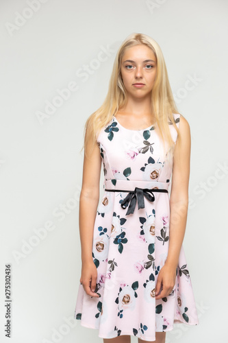 Portrait of a cute beautiful pretty woman girl with long beautiful hair on a white background in a pink dress with a pattern. Shows many different emotions, smiles and talks. Made in a studio.