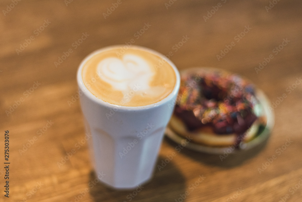 Coffee with a drawn heart and milk on a wooden table in a coffee shop. chocolate donut with scattering on the table next to the coffee Coffee with a drawn heart and milk on a wooden table in a coffee shop. chocolate donut with scattering on the table next to the coffee