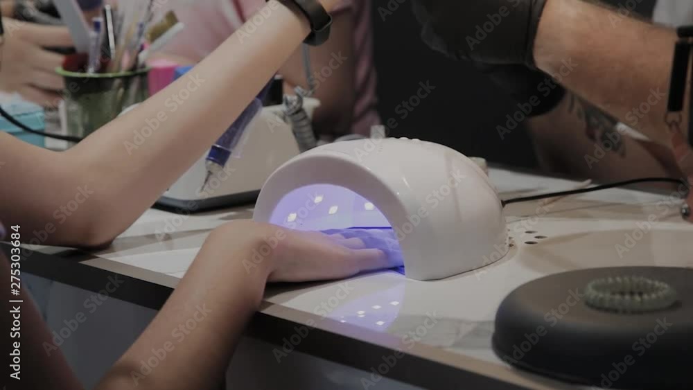 A young girl dries nail polish under an ultraviolet lamp in the manicure salon.
