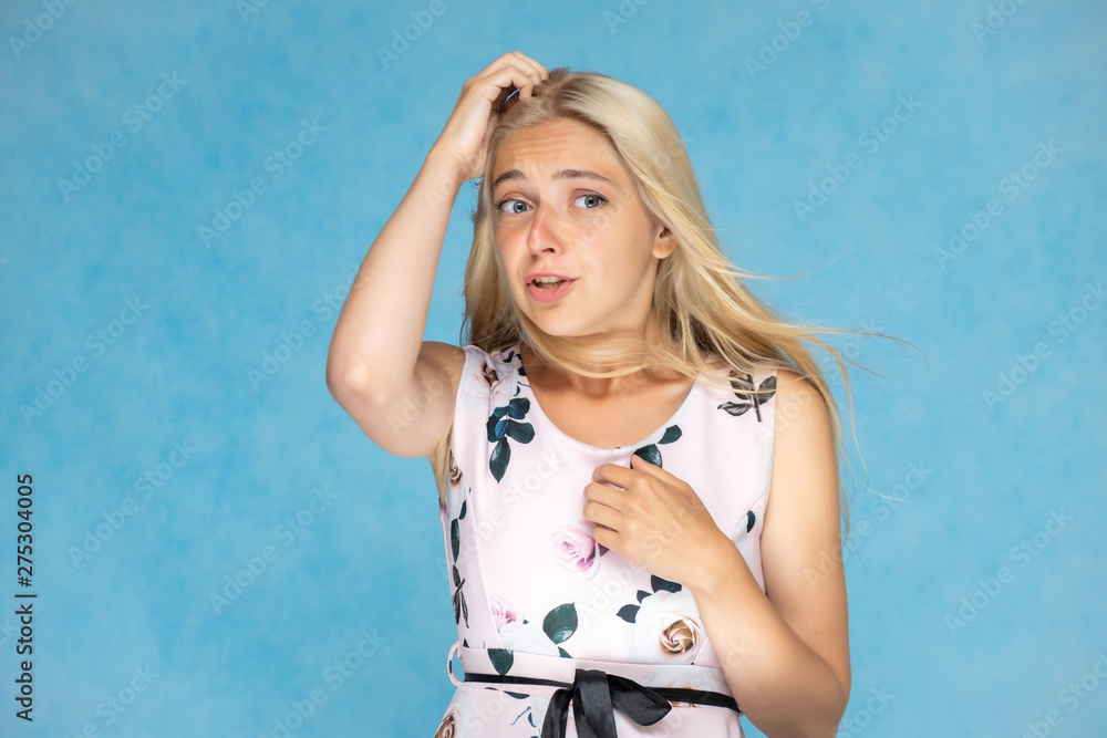 Portrait of a cute beautiful pretty woman girl with long beautiful hair on a blue background in a pink dress with a pattern. Shows a lot of different emotions, smiling, talking. Made in a studio. Portrait of a cute beautiful pretty woman girl with long beautiful hair on a blue background in a pink dress with a pattern. Shows a lot of different emotions, smiling, talking. Made in a studio.
