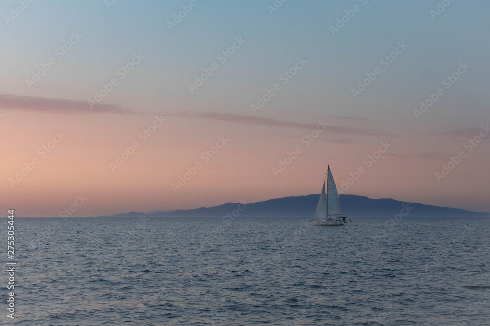 Fototapeta premium Sailboat on horizon with pink sunset