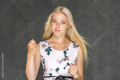 Portrait of a cute beautiful pretty woman girl with long beautiful hair on a dark gray background in a pink dress with a pattern. Shows a lot of different emotions, smiling, talking. Made in a studio.