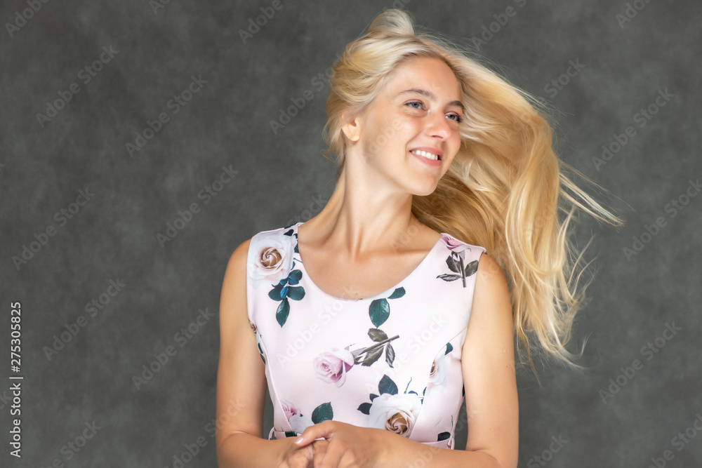 Portrait of a cute beautiful pretty woman girl with long beautiful hair on a dark gray background in a pink dress with a pattern. Shows a lot of different emotions, smiling, talking. Made in a studio. Portrait of a cute beautiful pretty woman girl with long beautiful hair on a dark gray background in a pink dress with a pattern. Shows a lot of different emotions, smiling, talking. Made in a studio.
