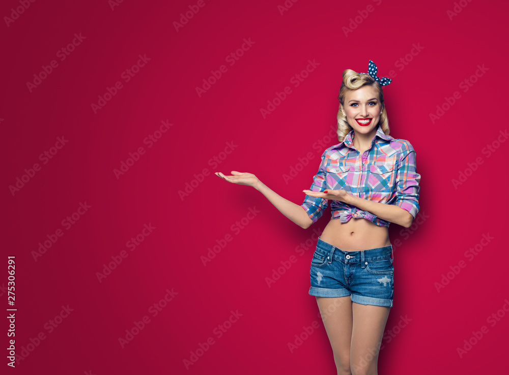 Photo of woman in pin up style, showing something or copyspace, over dark red background - obrazy, fototapety, plakaty 