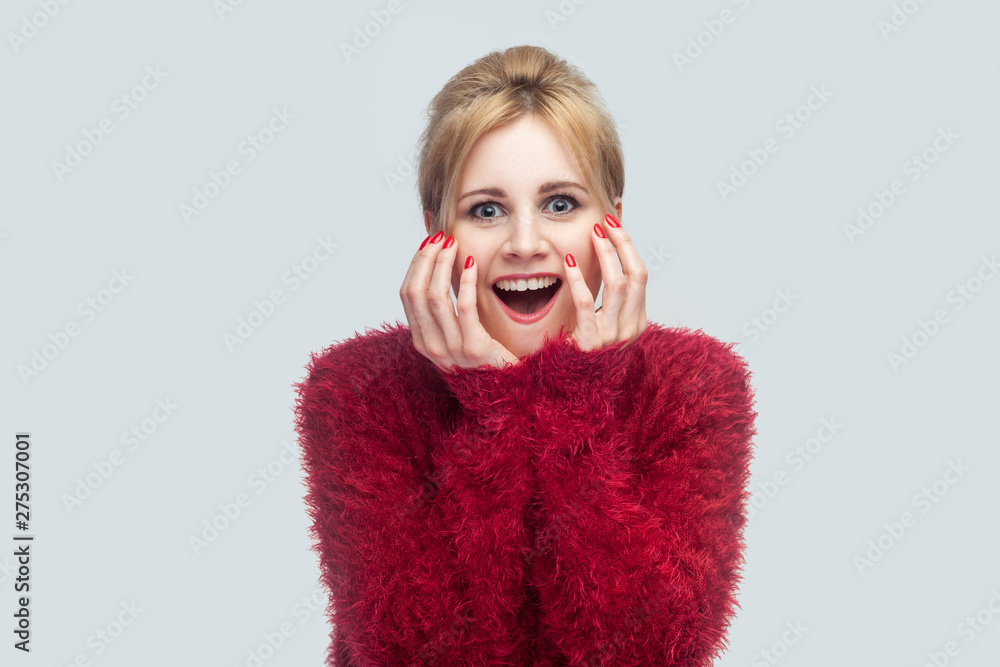Portrait of amazed beautiful young blond woman in red blouse standing and looking at camera with surprised face and happiness news touching face. indoor studio shot isolated on light gray background. Portrait of amazed beautiful young blond woman in red blouse standing and looking at camera with surprised face and happiness news touching face. indoor studio shot isolated on light gray background.