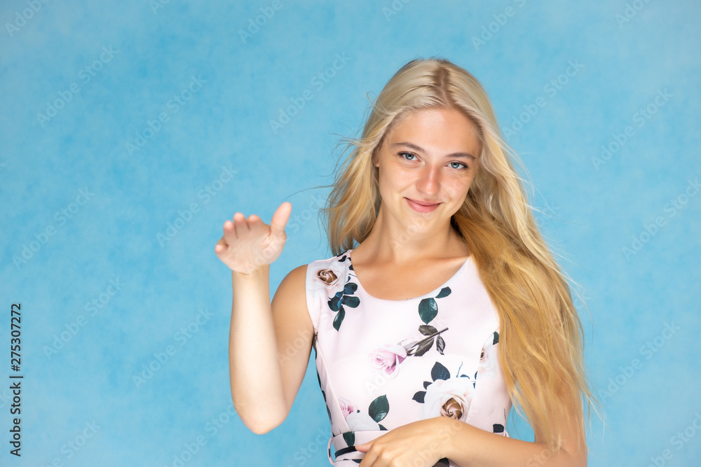 Portrait of a cute beautiful pretty woman girl with long beautiful hair on a blue background in a pink dress with a pattern. Shows a lot of different emotions, smiling, talking. Made in a studio.