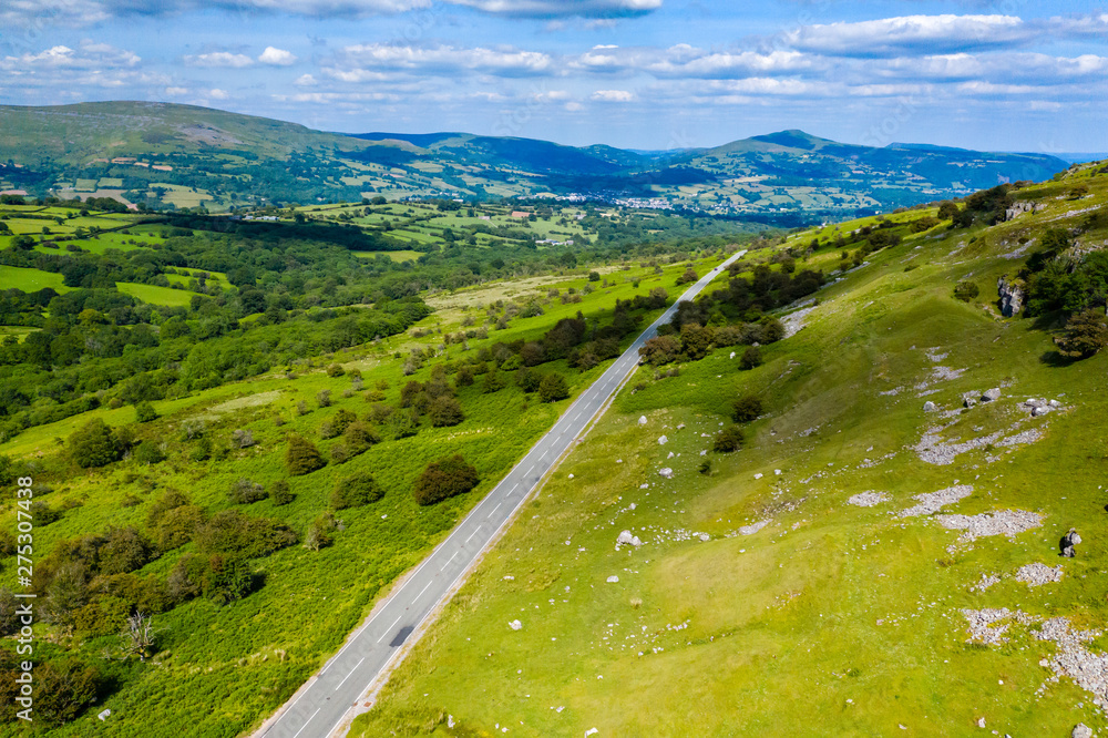 Aerial drone view of a rural road running through green farmland and rolling hills (Llangynidr, South Wales)