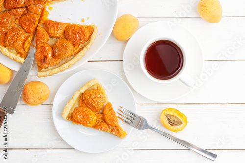 Homemade apricot pie with fresh fruits and cup of tea on white wooden table. Top view.