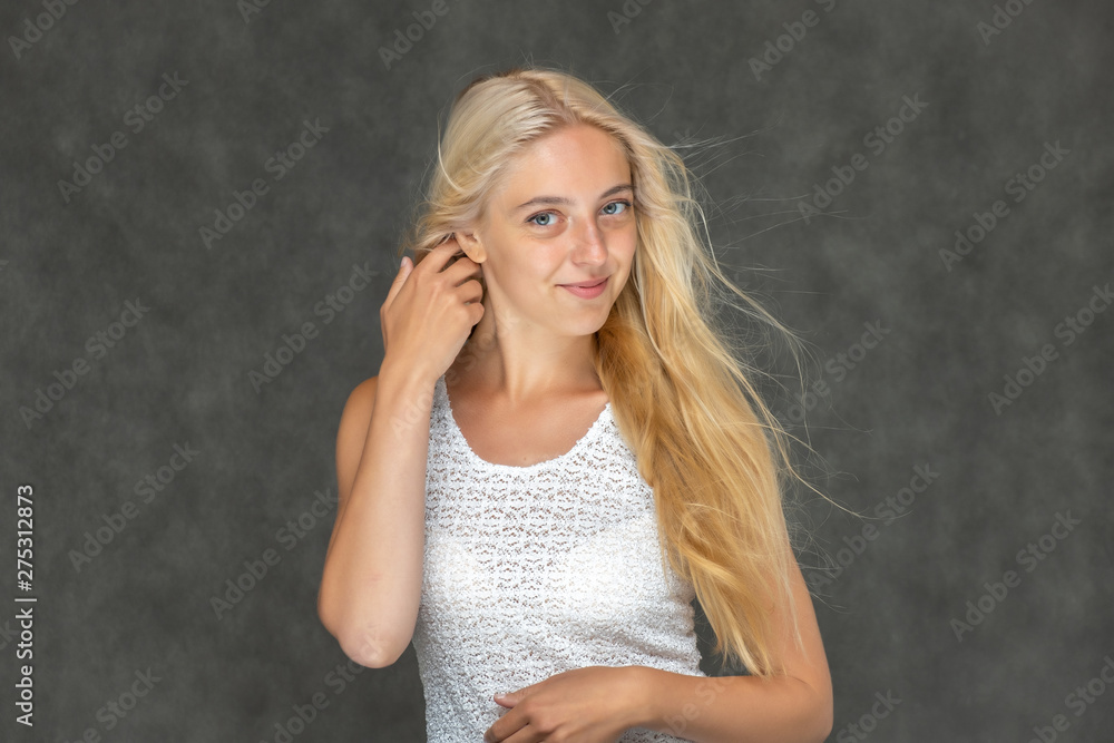 Portrait of a cute beautiful pretty woman girl with long beautiful hair on a dark gray background in a white sweater with a pattern. Shows many different emotions, smiles and talks. Made in a studio.