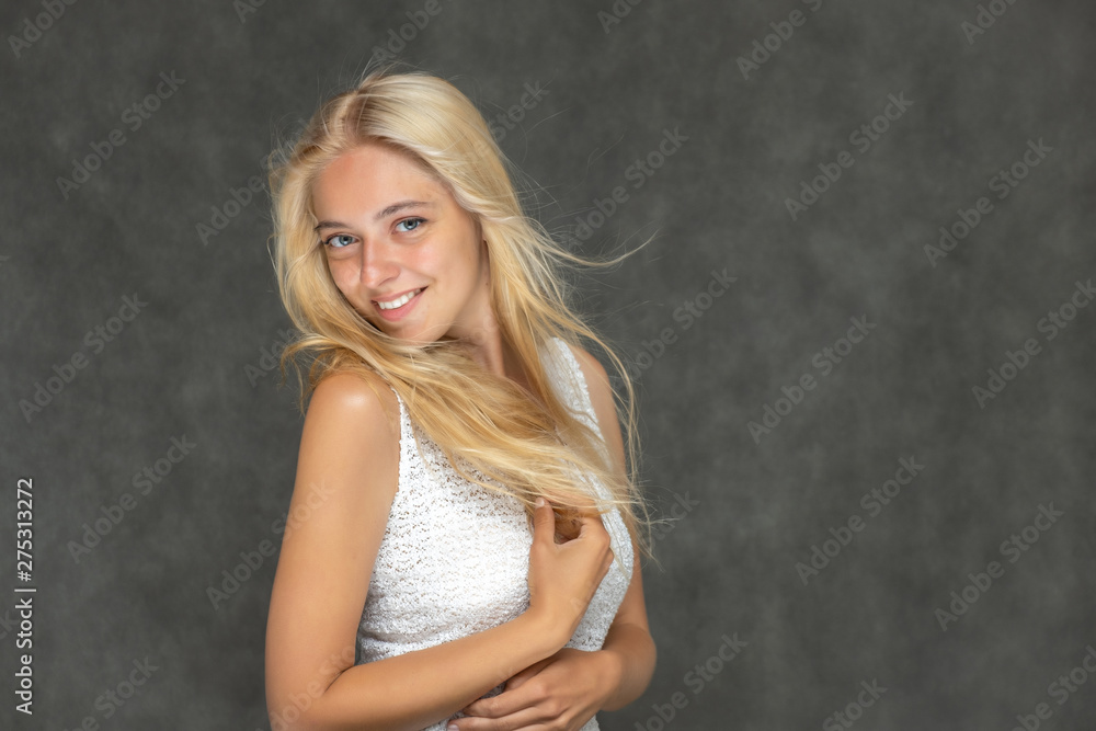 Portrait of a cute beautiful pretty woman girl with long beautiful hair on a dark gray background in a white sweater with a pattern. Shows many different emotions, smiles and talks. Made in a studio.