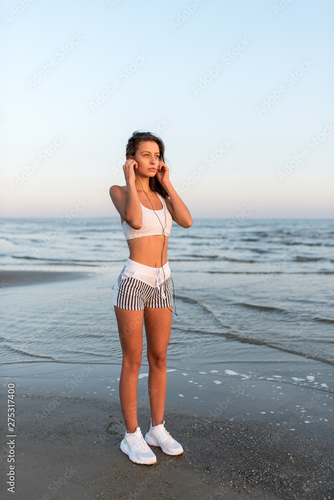 Sports fitness exercising woman on the beach listening to music