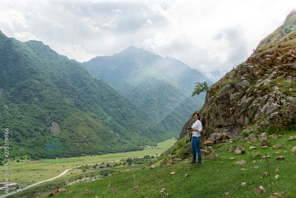 young woman in a white shirt and jeans stands against the mountain and looks at the valley. Photographer examines the landscape. Toned