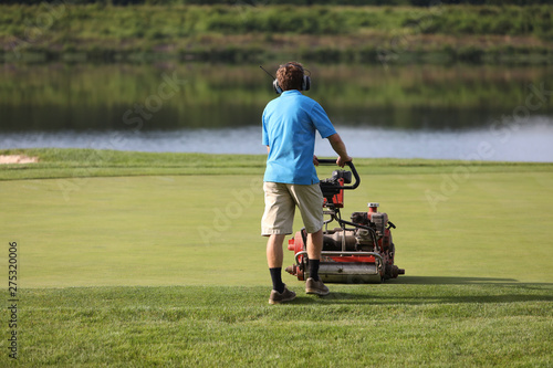 A young man cut the grass on a golf green in the early morning