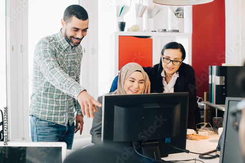 Canvas Print Happy male and female colleagues discussing over computer at desk in office