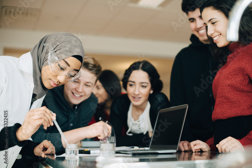 Canvas Print Smiling classmates looking at female student mixing solution during scientific e