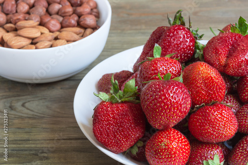 Plate of fresh strawberreis and almond, hazelnut on wooden background. Vegetarian breakfast photo