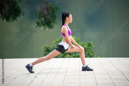 Fototapeta Naklejka Na Ścianę i Meble -  Fitness girl exercising outdoor in urban city architecture, stretching legs, doing squash, push-buttons, jumps, resting, smiling athlete body