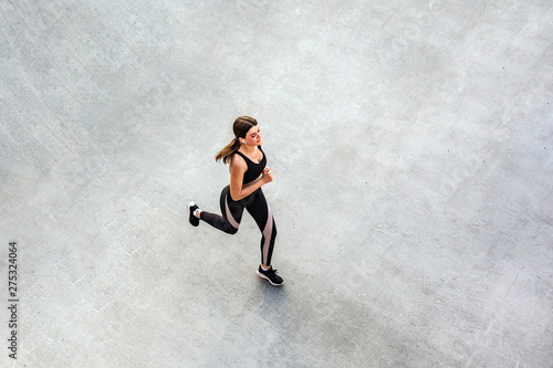 Top view of young attractive athletic woman speed running on city asphalt and workout in the morning time on a sunny summer day. Female runner training outdoor. Copyspace, sport concept