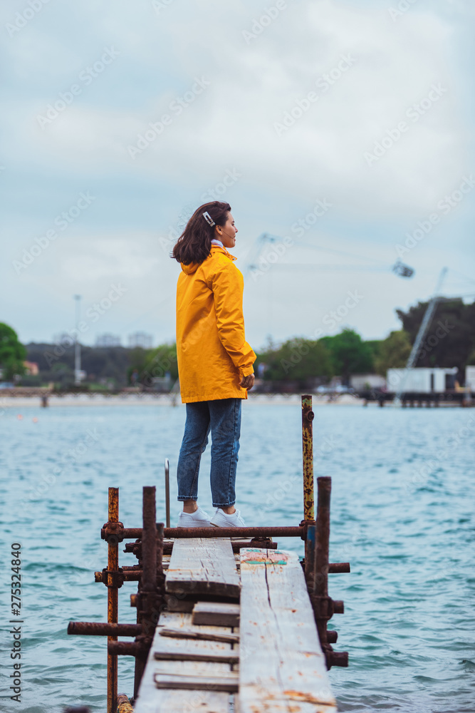 woman in yellow raincoat at sea pier looking at storming water