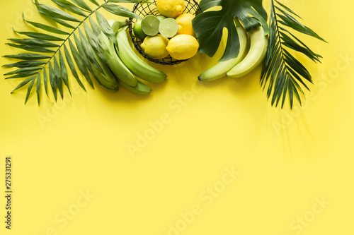 Tropical border of fruits, banana, lime, leaves palms on punchy yellow background. Space for text. Detox tour. photo