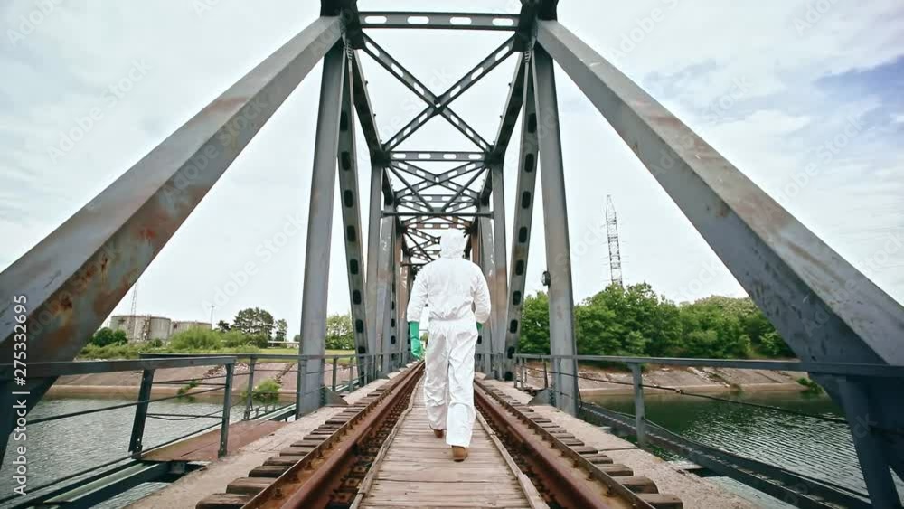 Back view of white stalker walking on abandoned useless bridge in high radiation exclusion zone. Tour to Chernobyl power plant and surroundings in hot summer. Back view of white stalker walking on abandoned useless bridge in high radiation exclusion zone. Tour to Chernobyl power plant and surroundings in hot summer.