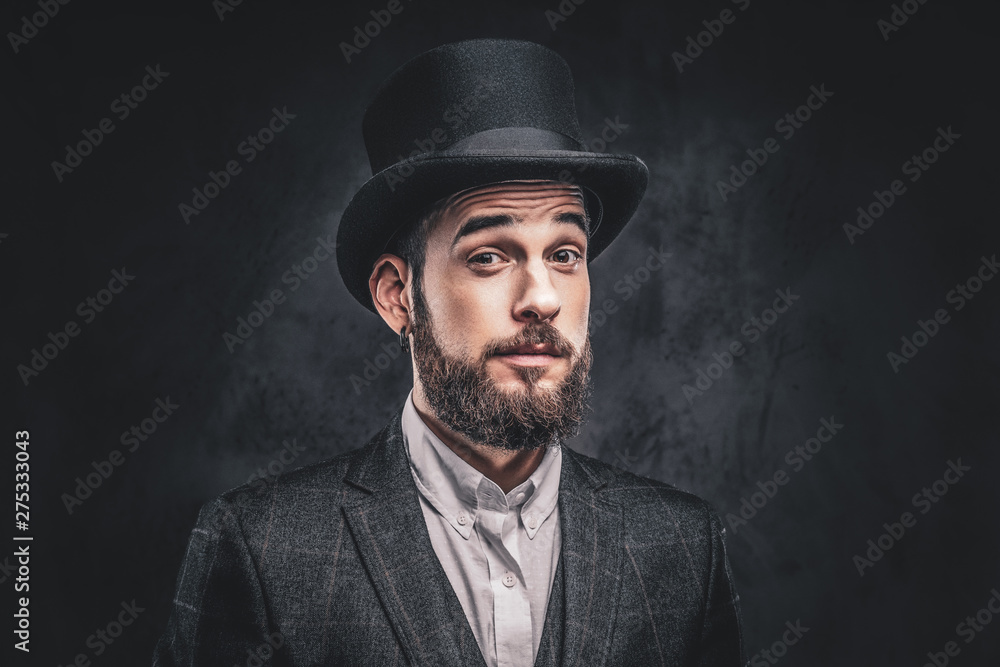 Portrait of a stylish bearded male in an elegant suit and cylinder hat, looking at a camera over dark background. Portrait of a stylish bearded male in an elegant suit and cylinder hat, looking at a camera over dark background.