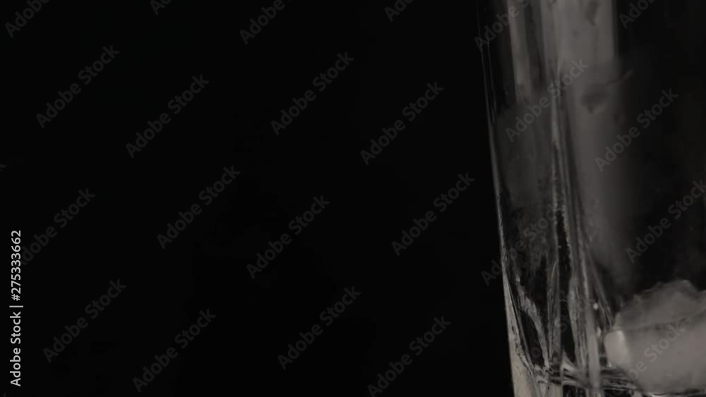 A drop of water flows down the side of a whiskey glass on a black background A drop of water flows down the side of a whiskey glass on a black background