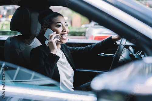 Happy woman in formal wear enjoying road driving in to financial district and online cell call conversation with friend connected to roaming internet in car, cheerful female expert talking via app © BullRun