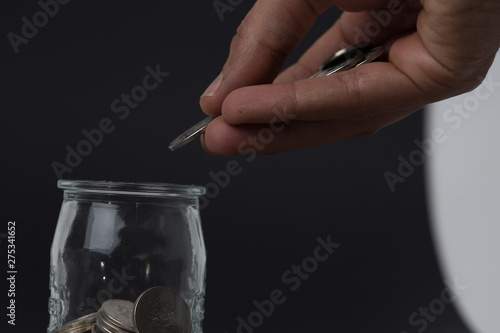 Hand putting coin into glass container coins in a glass jar against  savings coins - Investment And Interest Concept saving money concept  growing money on piggy bank. isolated on white background
